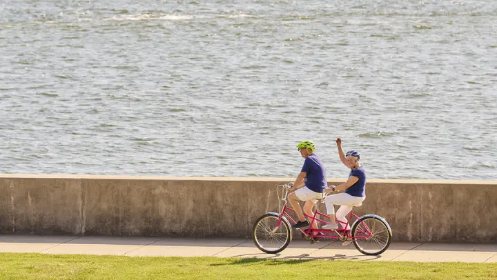 Two people riding tandem bicycle by waterfront