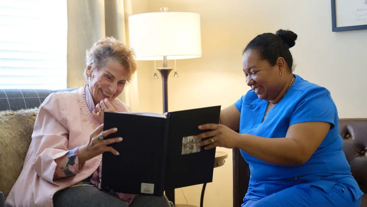 Two women smiling at photo album indoors